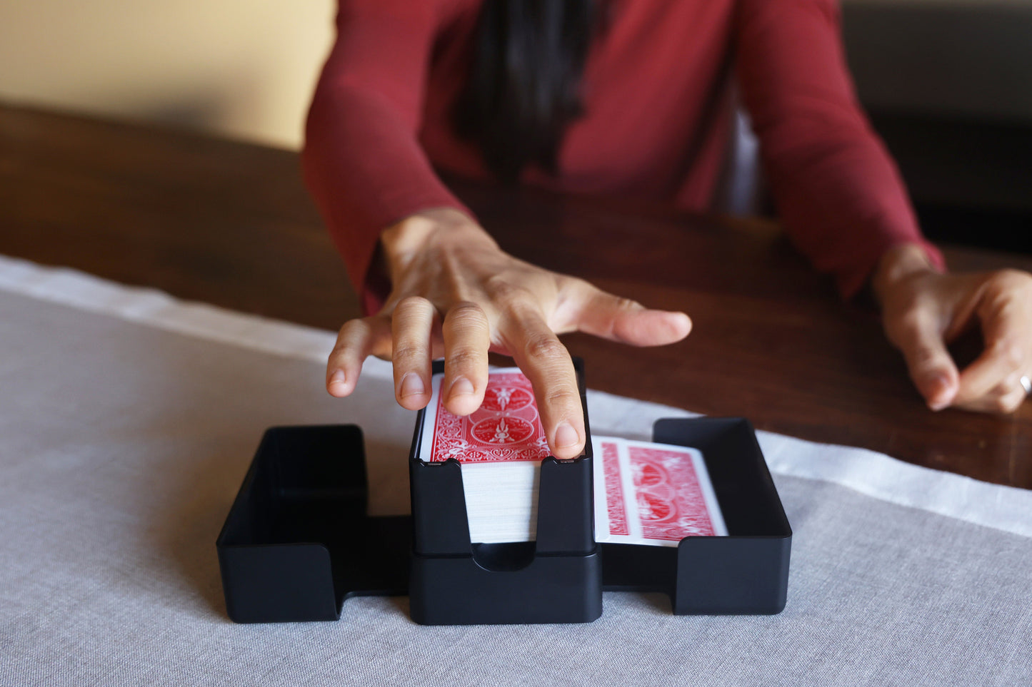 A person at a wooden table tapping the Lotus card shuffler during a game