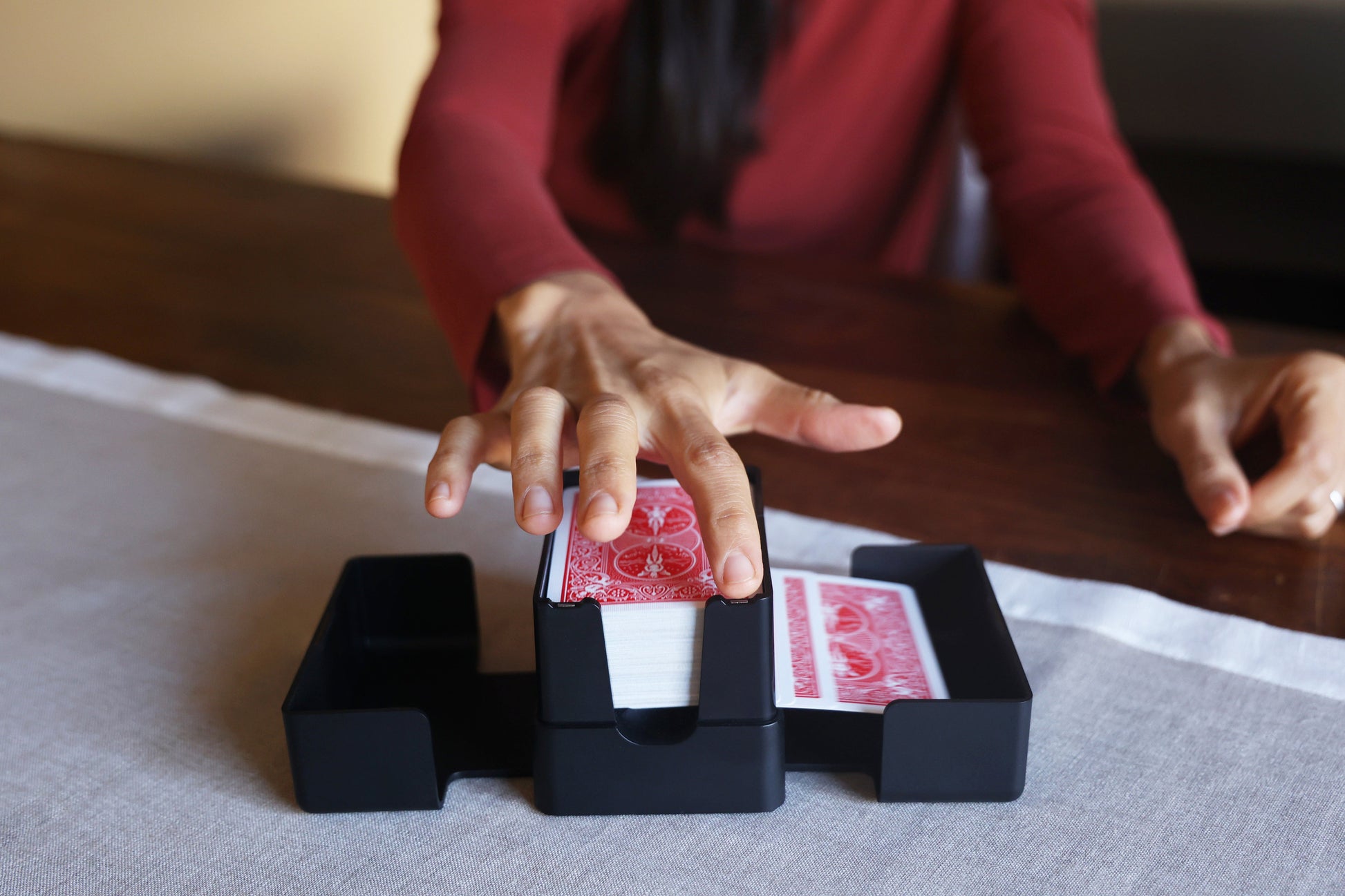 A person at a wooden table tapping the Lotus card shuffler during a game